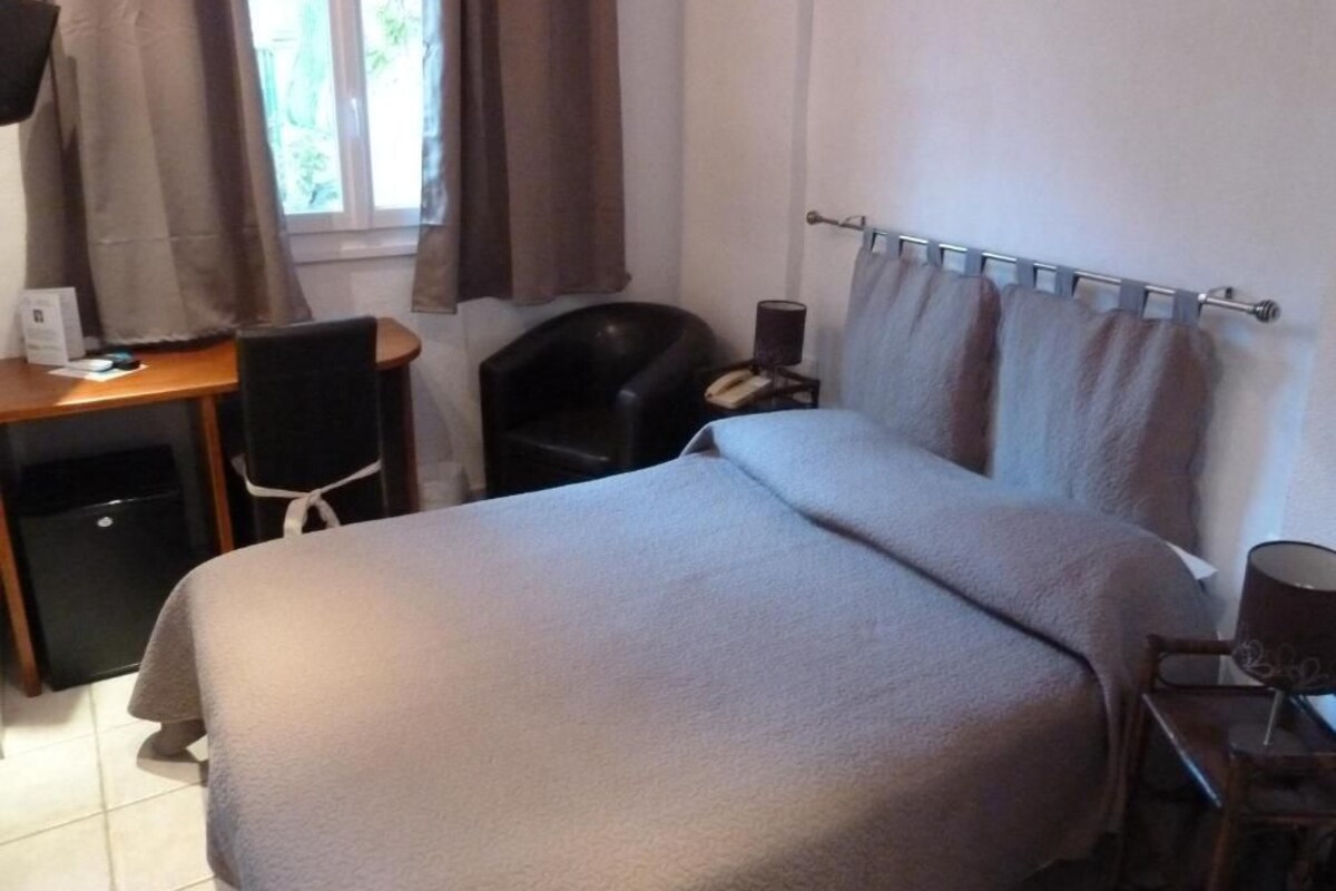 Una habitación de hotel con cama, escritorio, silla, teléfono y ventana con cortinas.