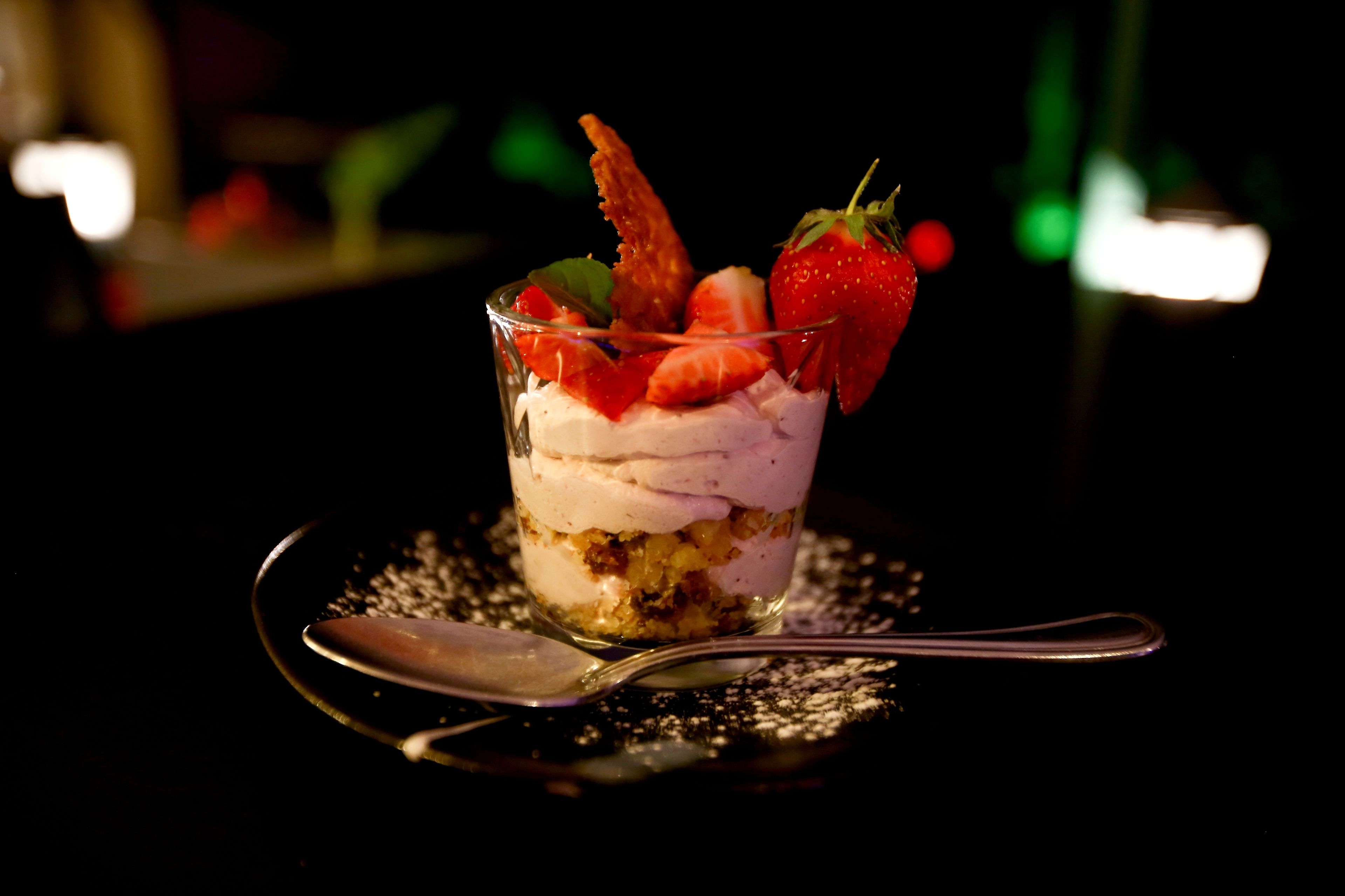 A dessert in a clear glass with strawberries and whipped cream.