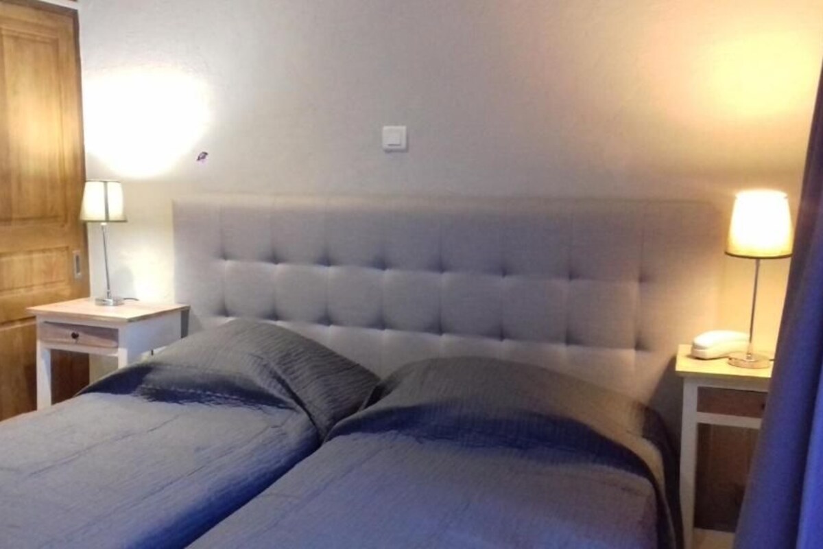 Un dormitorio con cabecera capitonada, dos mesitas de noche con lámparas y una puerta de madera.
