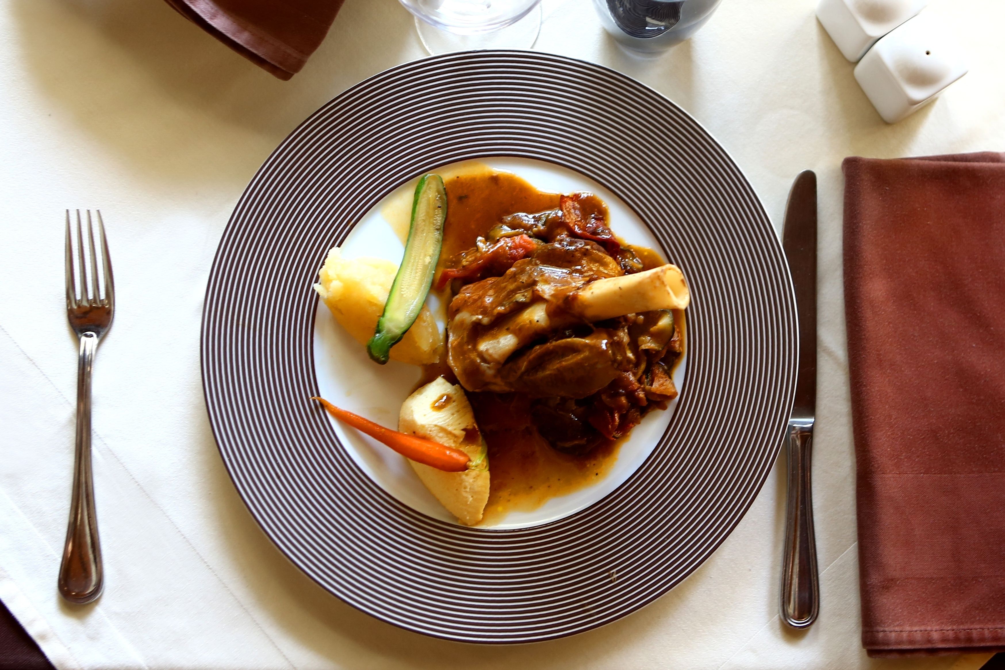 A plate of food with a striped rim, accompanied by a fork and knife on a tablecloth.