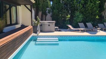 A swimming pool with lounge chairs, a hot tub, and wooden deck.