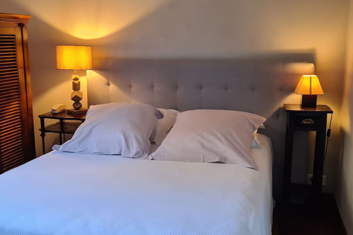 A neatly made bed with white linens and two pillows, flanked by wooden nightstands with lamps.