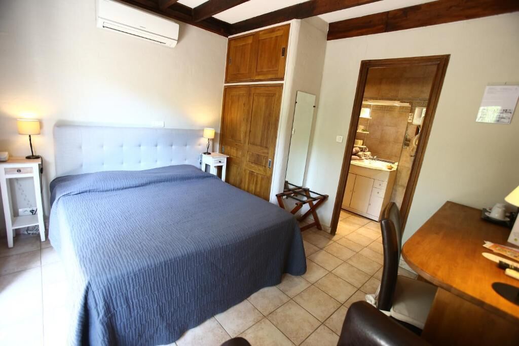 Un dormitorio con cama, mesitas de noche, un armario de madera, una pequeña mesa de comedor y una zona de cocina.