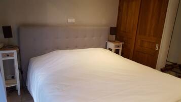 A bedroom with a large bed, a nightstand with a lamp, and a wooden door.