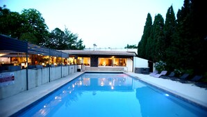 Una piscina con sillones de descanso y un edificio con un patio techado.