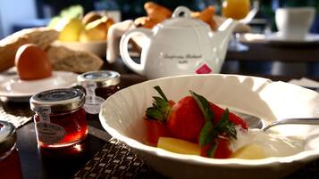 A breakfast setting with a bowl of fruit, a teapot, and a jar of jam.