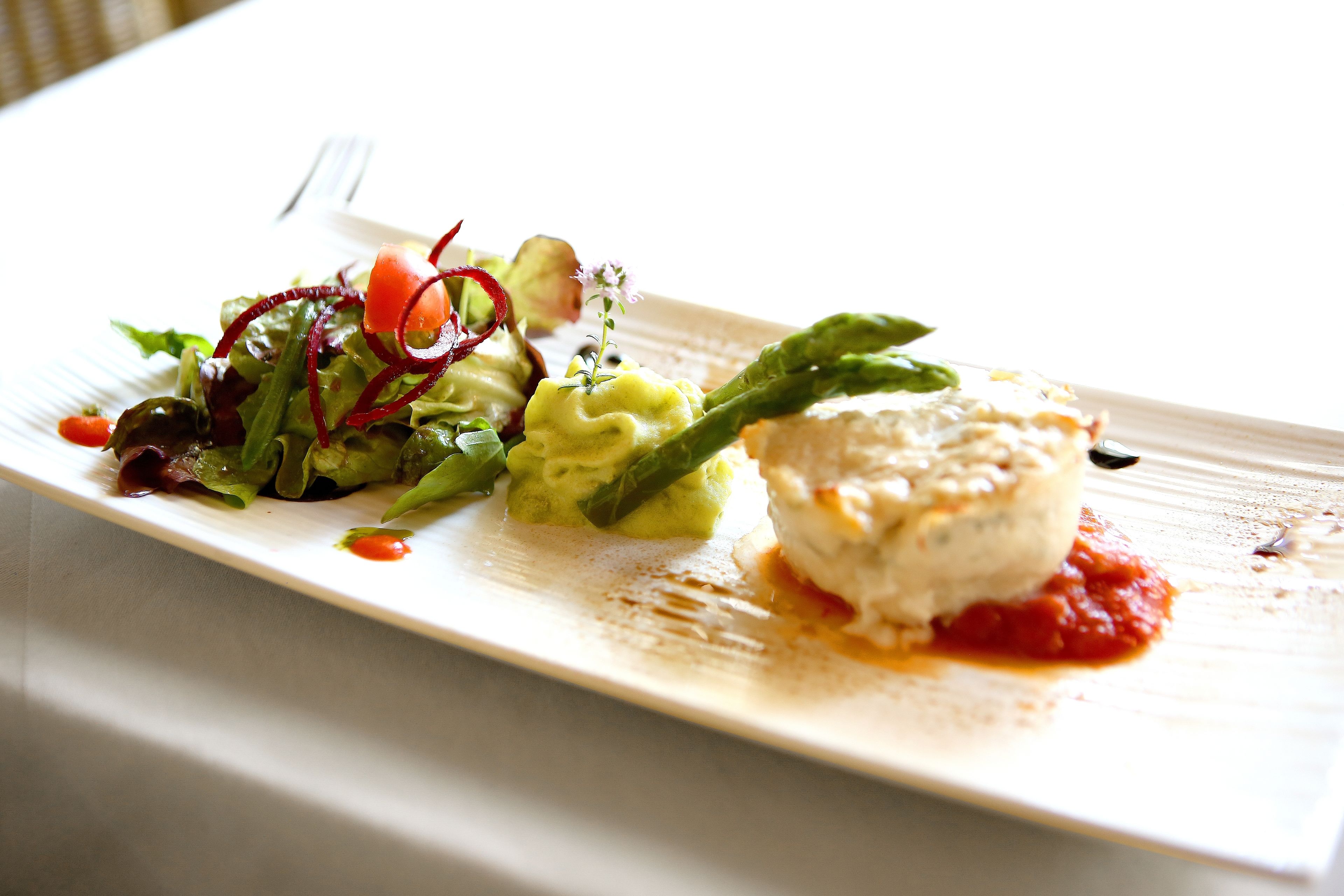 Une assiette blanche contenant divers aliments, notamment un morceau de poisson, un légume vert et une salade.