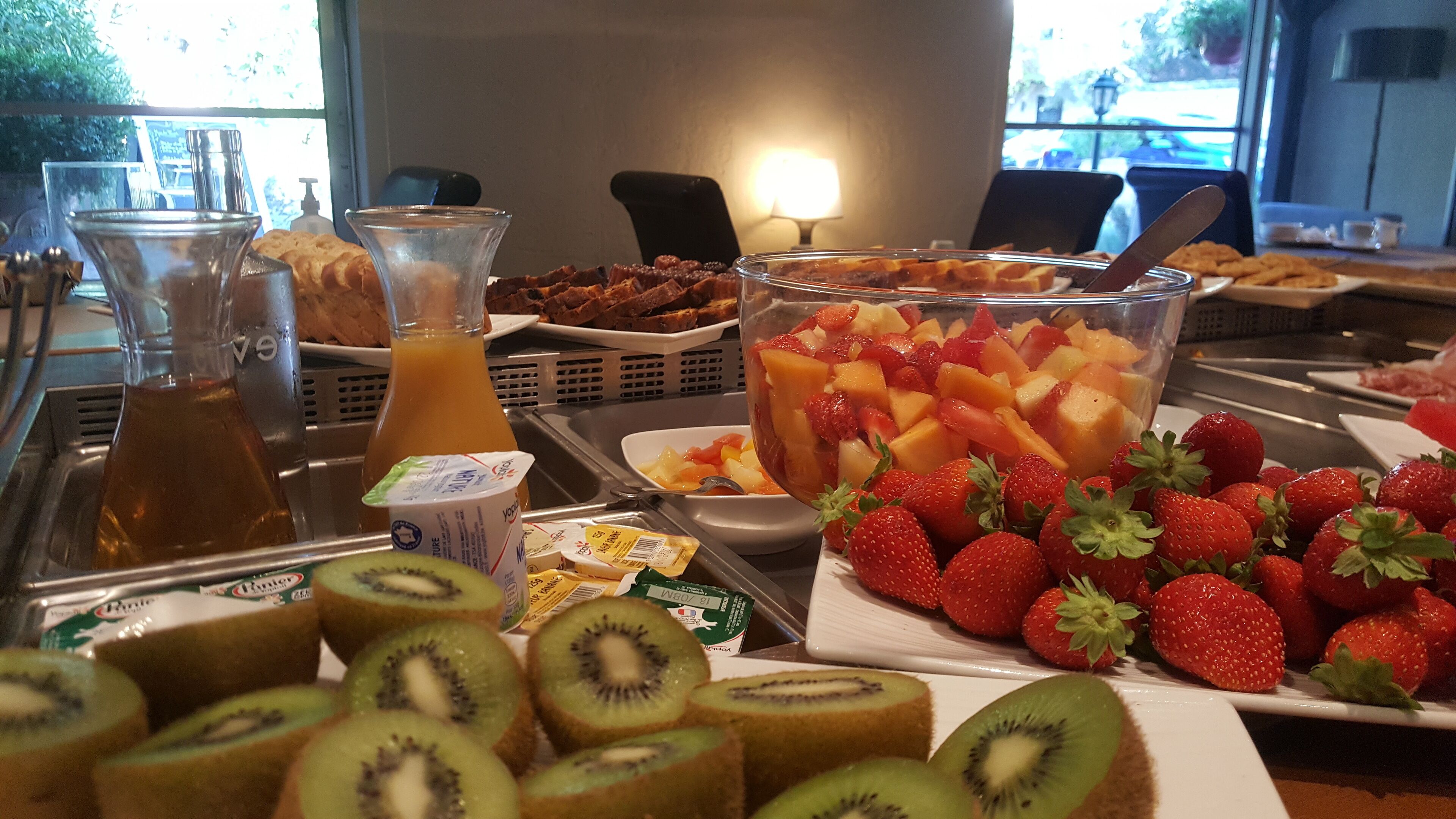 A breakfast buffet with various fruits, yogurt, and juice.
