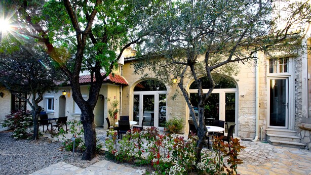 Un patio con suelo de piedra, mobiliario exterior y un edificio de fachada de piedra y ventanas de arco.