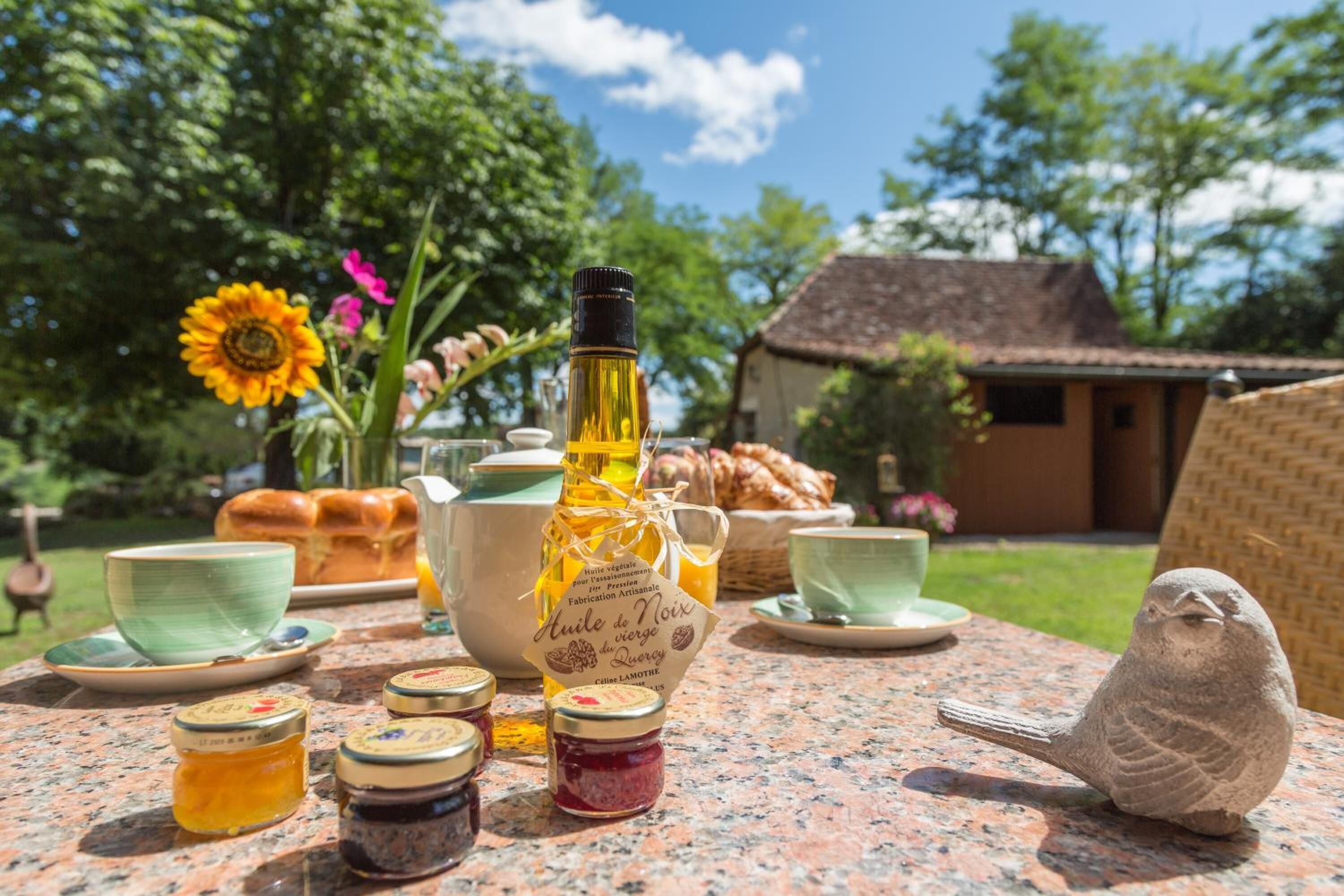 A table set with a bottle of honey, jars of jam, a bird sculpture, and a sunflower arrangement.