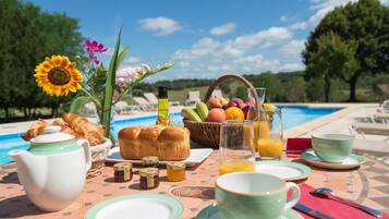 Desayuno junto a una piscina con cruasanes, pan, fruta y jugo.