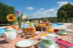 Desayuno junto a una piscina con cruasanes, pan, fruta y jugo.