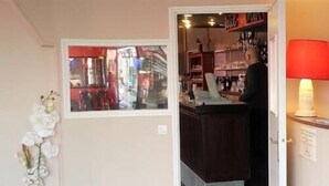 A hotel room with a view of a street through a window, a reception desk, a lamp, and a white orchid plant. - Hôtel Restaurant Le Hussard (Alencon)