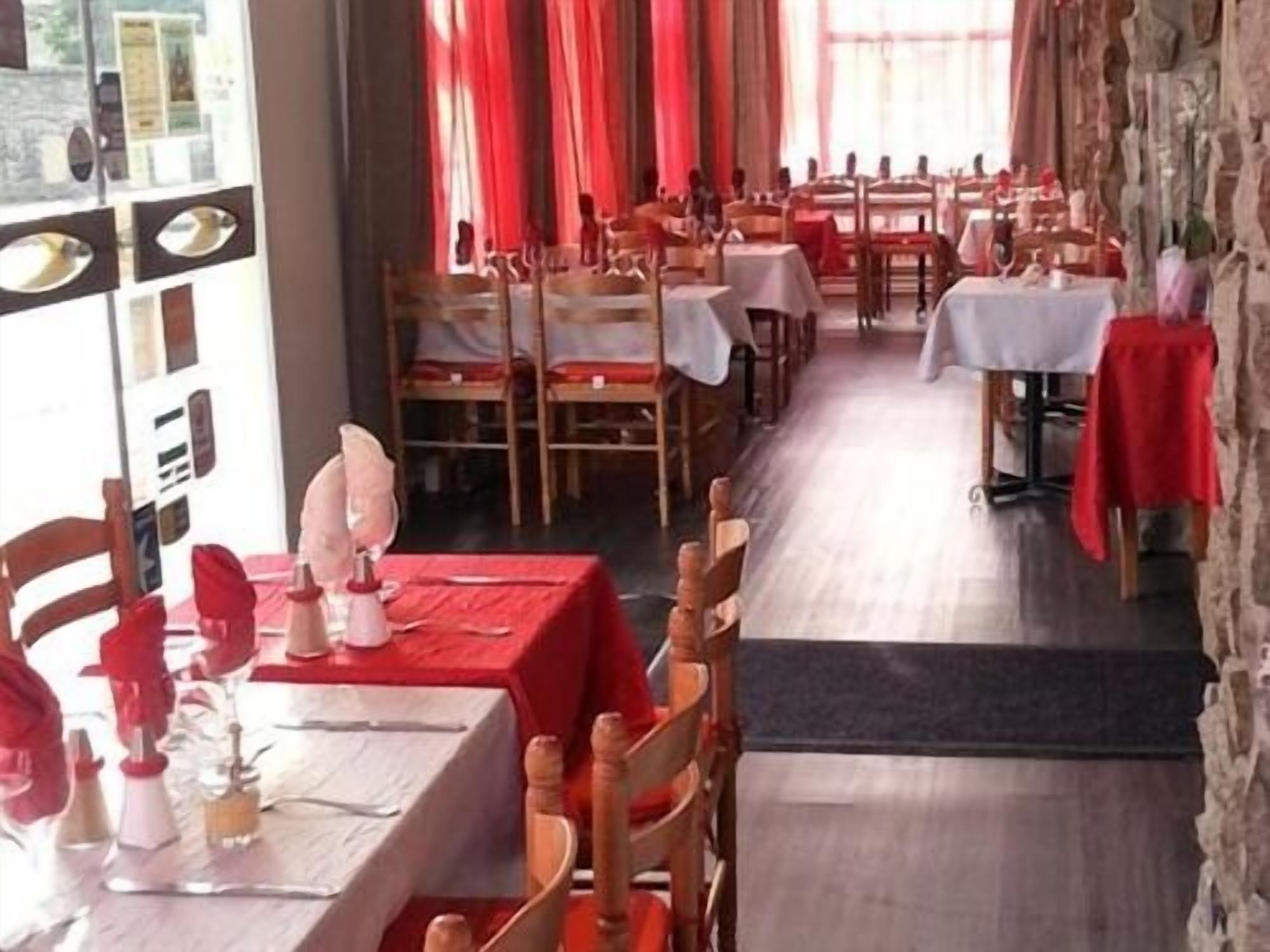 A restaurant with multiple tables and chairs, red tablecloths, and a stone wall.