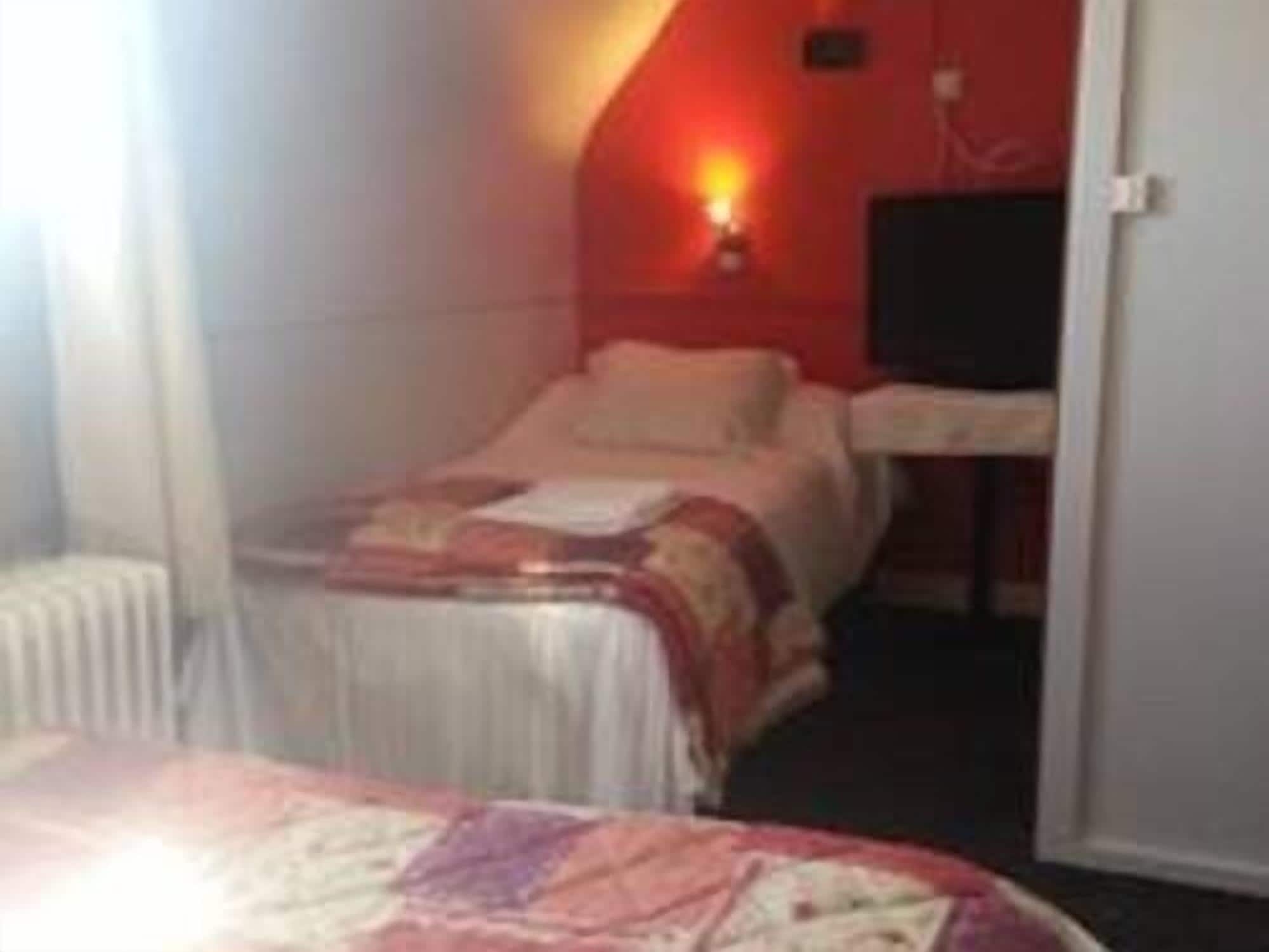 Una habitación pequeña con cama individual, pared de acento roja, mesita de noche y ventana.