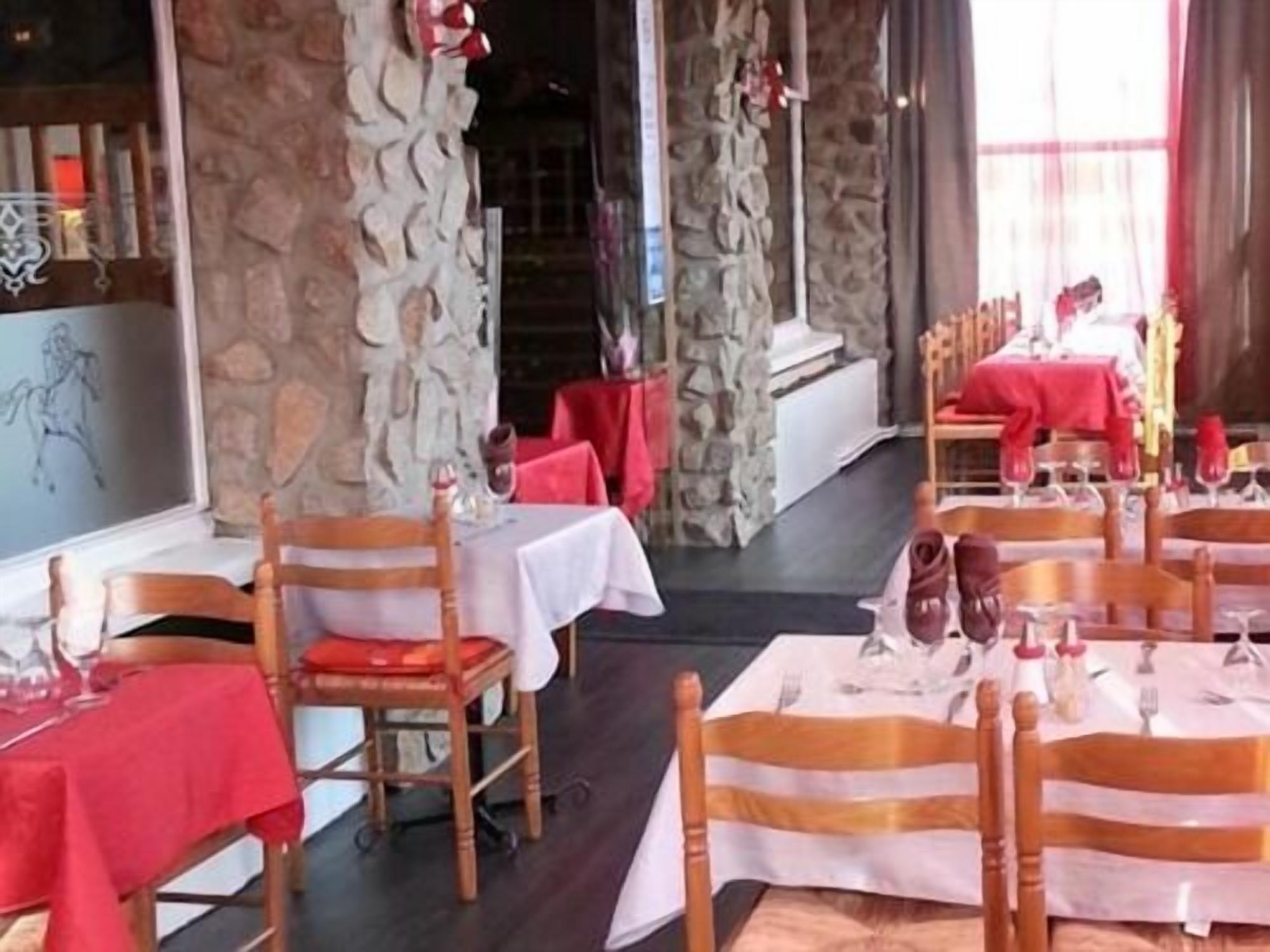 A restaurant with wooden chairs and tables, stone walls, and red tablecloths.