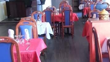 Een restaurant met meerdere tafels en stoelen, waarvan sommige bedekt zijn met rode tafelkleden.