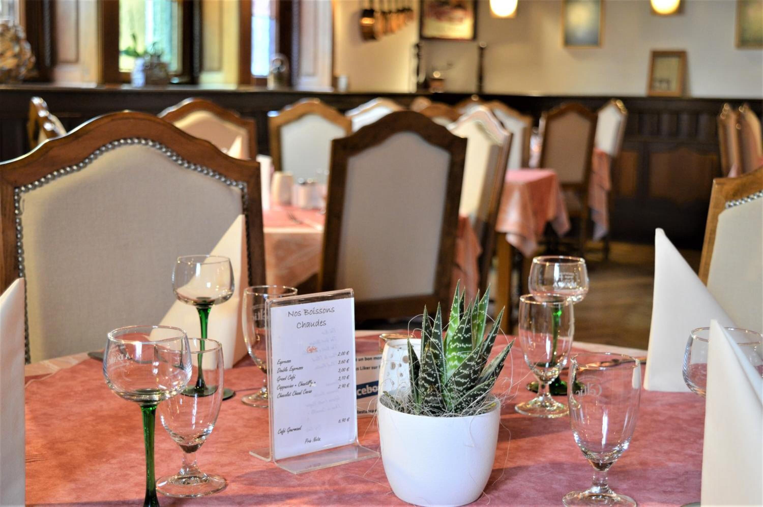 A restaurant table set with wine glasses, a menu, and a potted plant.