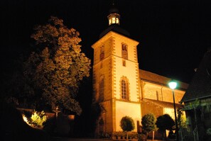 Un bâtiment historique doté d’une tour imposante et de fenêtres en arc de cercle, entouré d’arbres et d’un lampadaire.