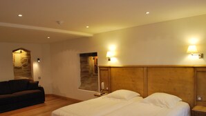 Habitación de hotel con cama, cabecero de madera, mesita de noche, lámpara, teléfono en la pared y pared de piedra.
