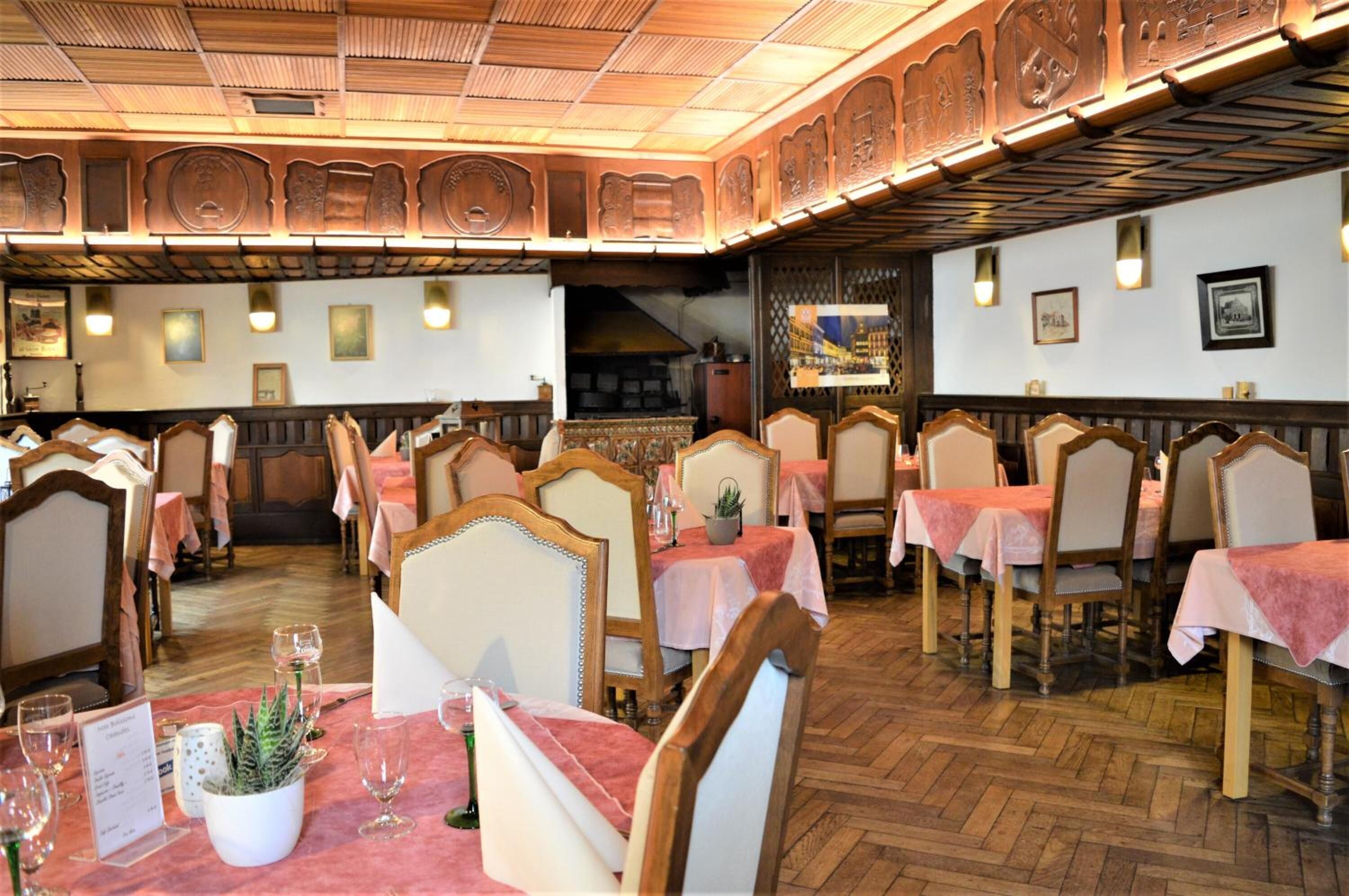 Un restaurant avec des meubles en bois, des nappes roses et un parquet à motifs en chevrons.
