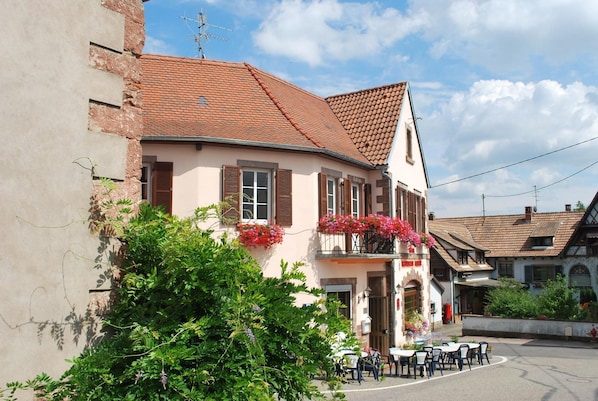 A traditional building with a sloped roof, a balcony with flowers, and outdoor seating. - Kleiber (Saint-Jean-Saverne)