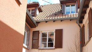 Un patio con mobiliario exterior, techo de baldosas y un edificio con ventanas arqueadas.