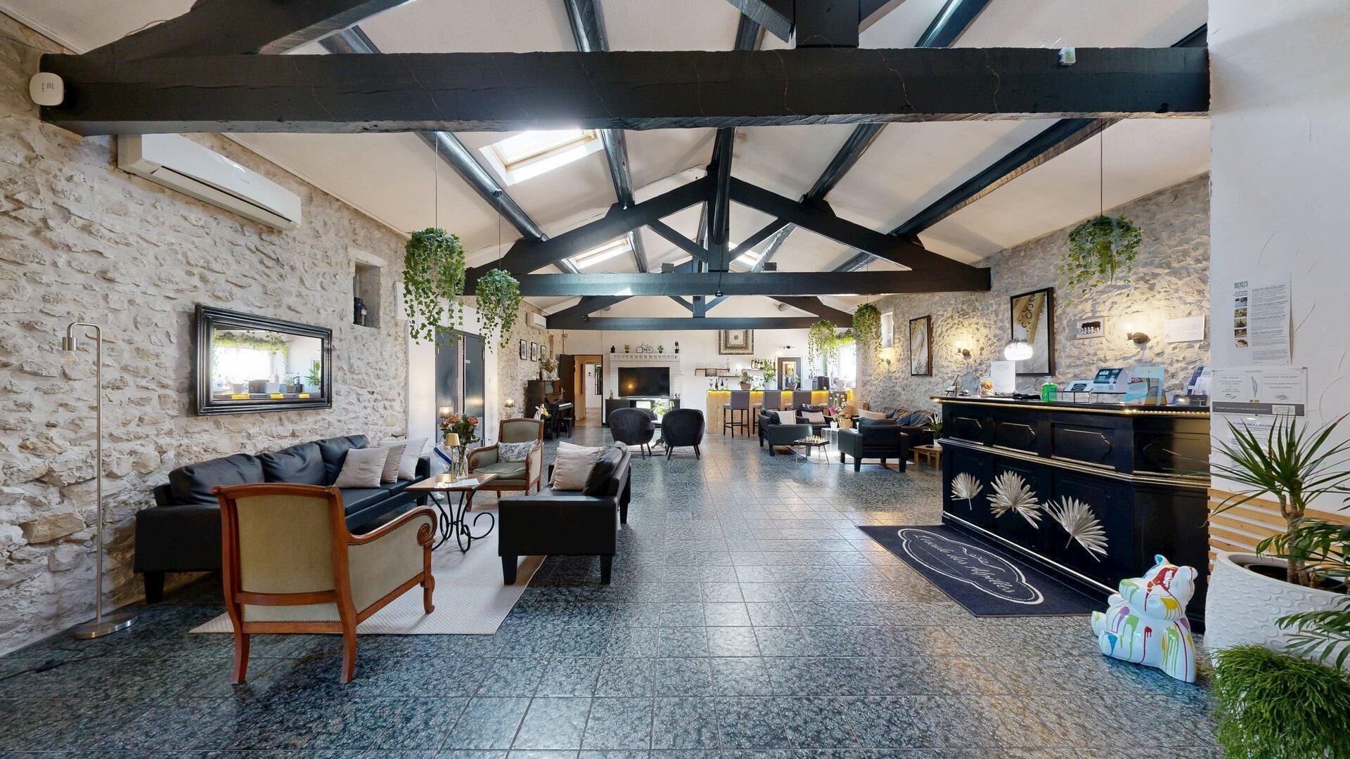 A spacious hotel lobby with stone walls, a high ceiling with exposed beams, a reception desk, seating areas, and a fireplace.