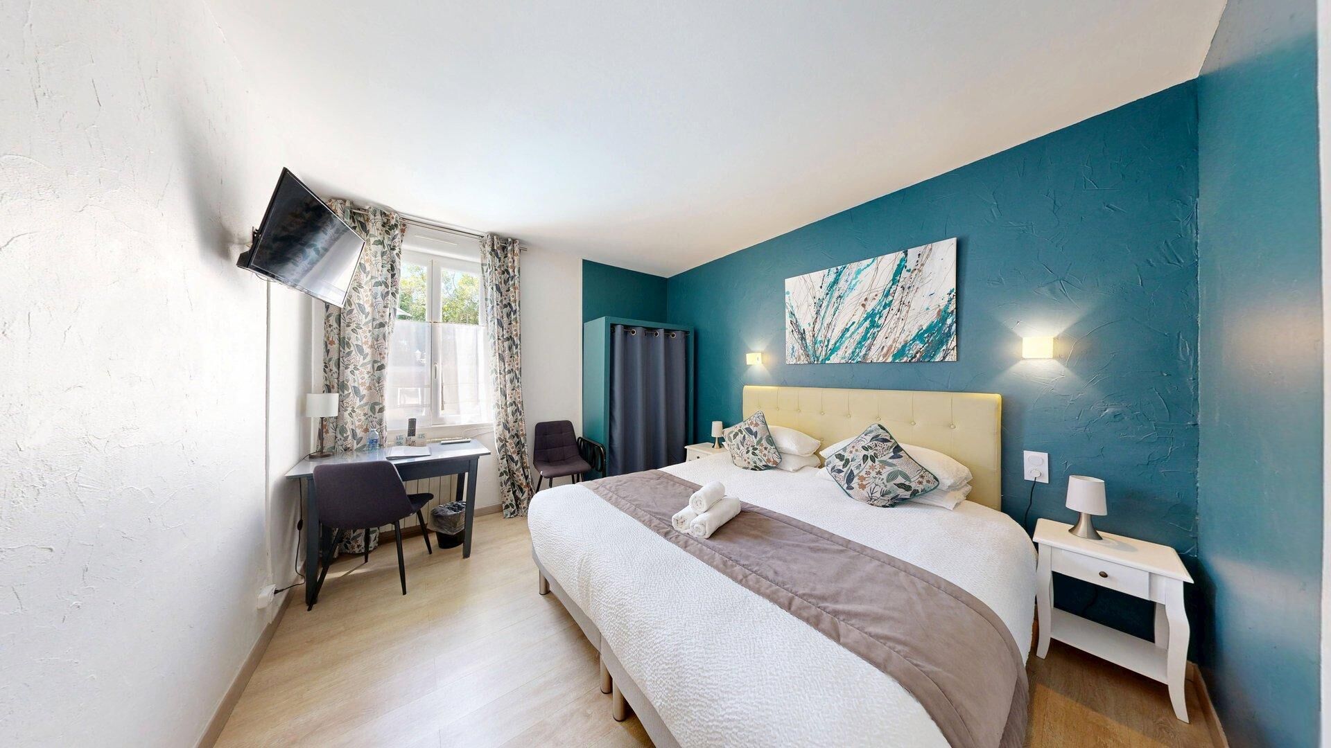 A bedroom with a bed, desk, chair, and a painting on the wall.