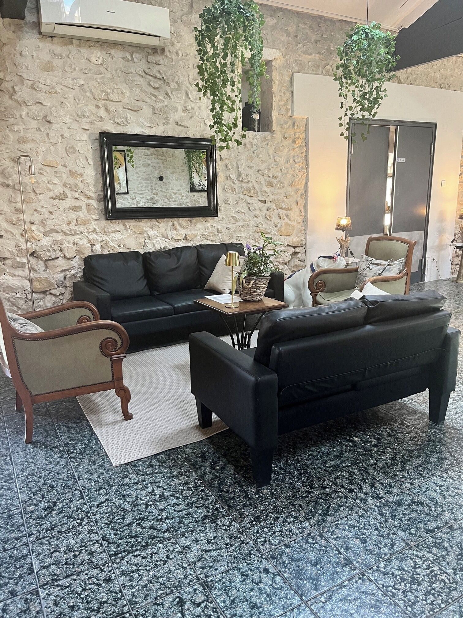 Ein Wohnzimmer mit einer Steinwand, einem schwarzen Ledersofa, einem Holzstuhl, einem Couchtisch und hängenden Pflanzen.