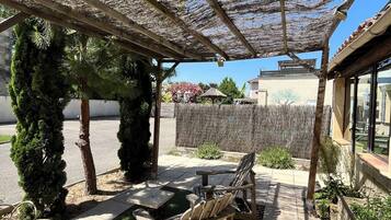 Un espace extérieur aménagé, abrité et doté de mobilier en bois, d’une pergola et d’une végétation luxuriante.