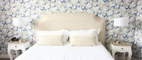 Una habitación de hotel con una cama grande, dos mesitas de noche con lámparas, y un papel tapiz estampado.