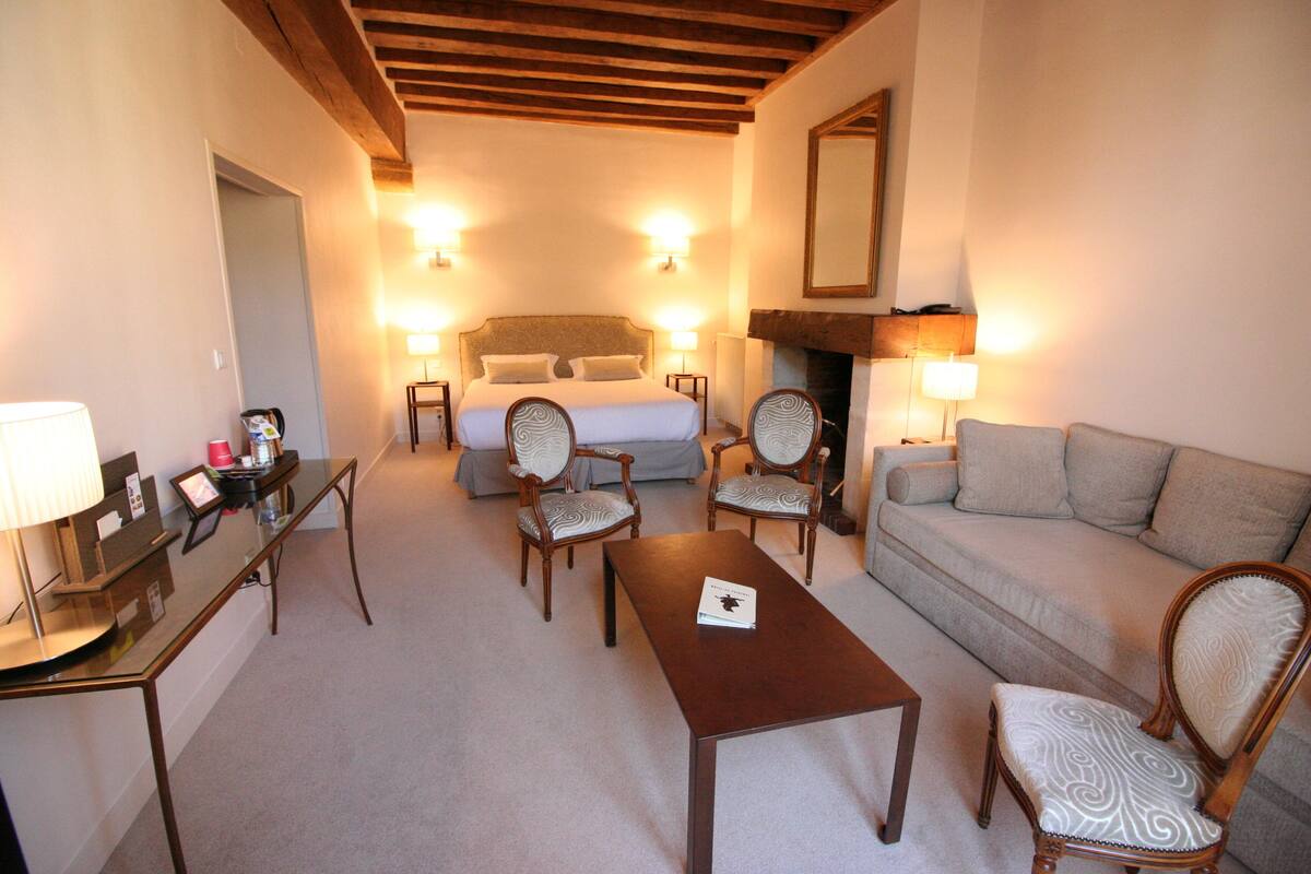 A hotel room with a bed, two armchairs, a sofa, a table, and a desk with a lamp.