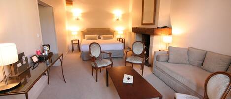 A hotel room with a bed, two armchairs, a sofa, a table, and a desk with a lamp.
