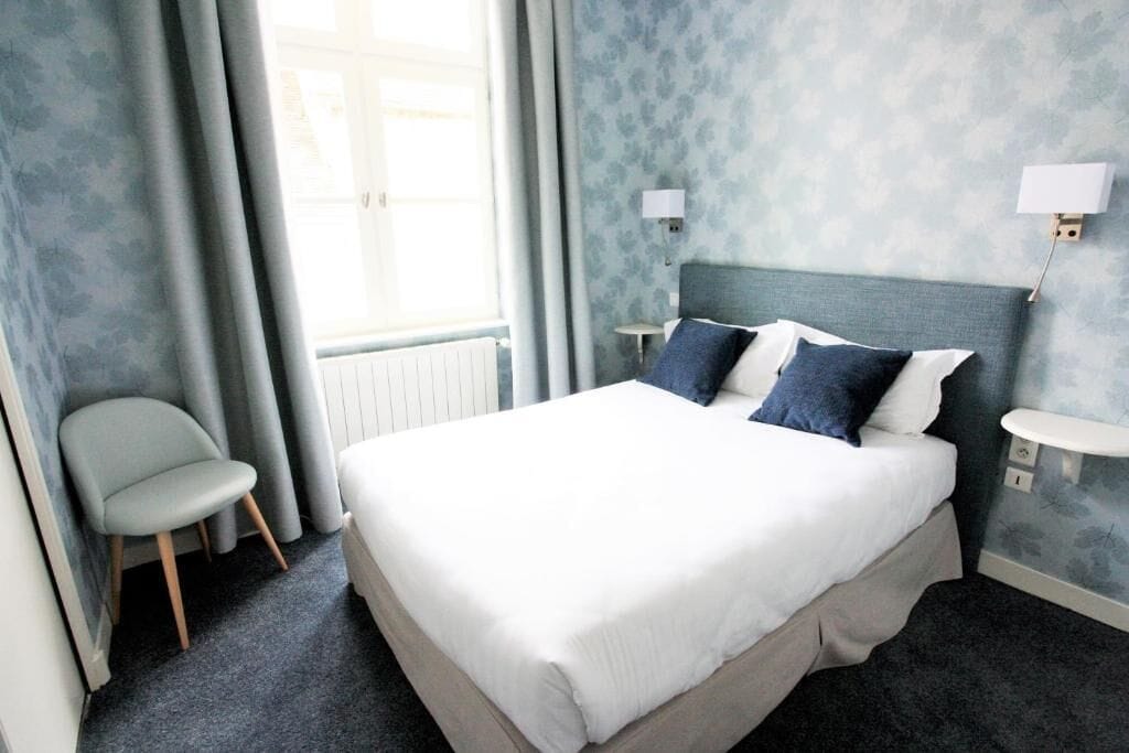 Ein Hotelzimmer mit einem Bett, einem Sessel, einem Nachttisch und einer Wandlampe.