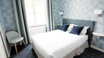 Una habitación de hotel con una cama, una silla, una mesita de noche y una lámpara de pared.