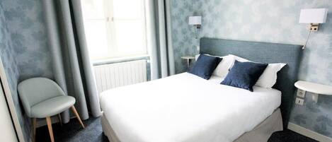 Ein Hotelzimmer mit einem Bett, einem Sessel, einem Nachttisch und einer Wandlampe.