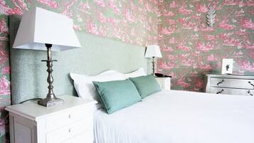 A neatly made bed with white and green bedding, a white nightstand with a lamp, and a dresser with a mirror.