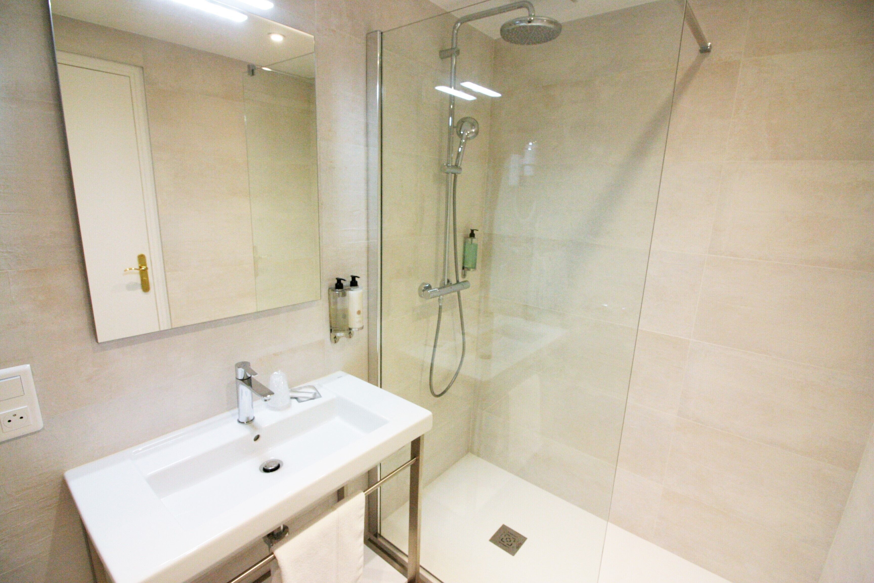 A modern bathroom with a glass-enclosed shower, a white sink, and a mirror above the sink.