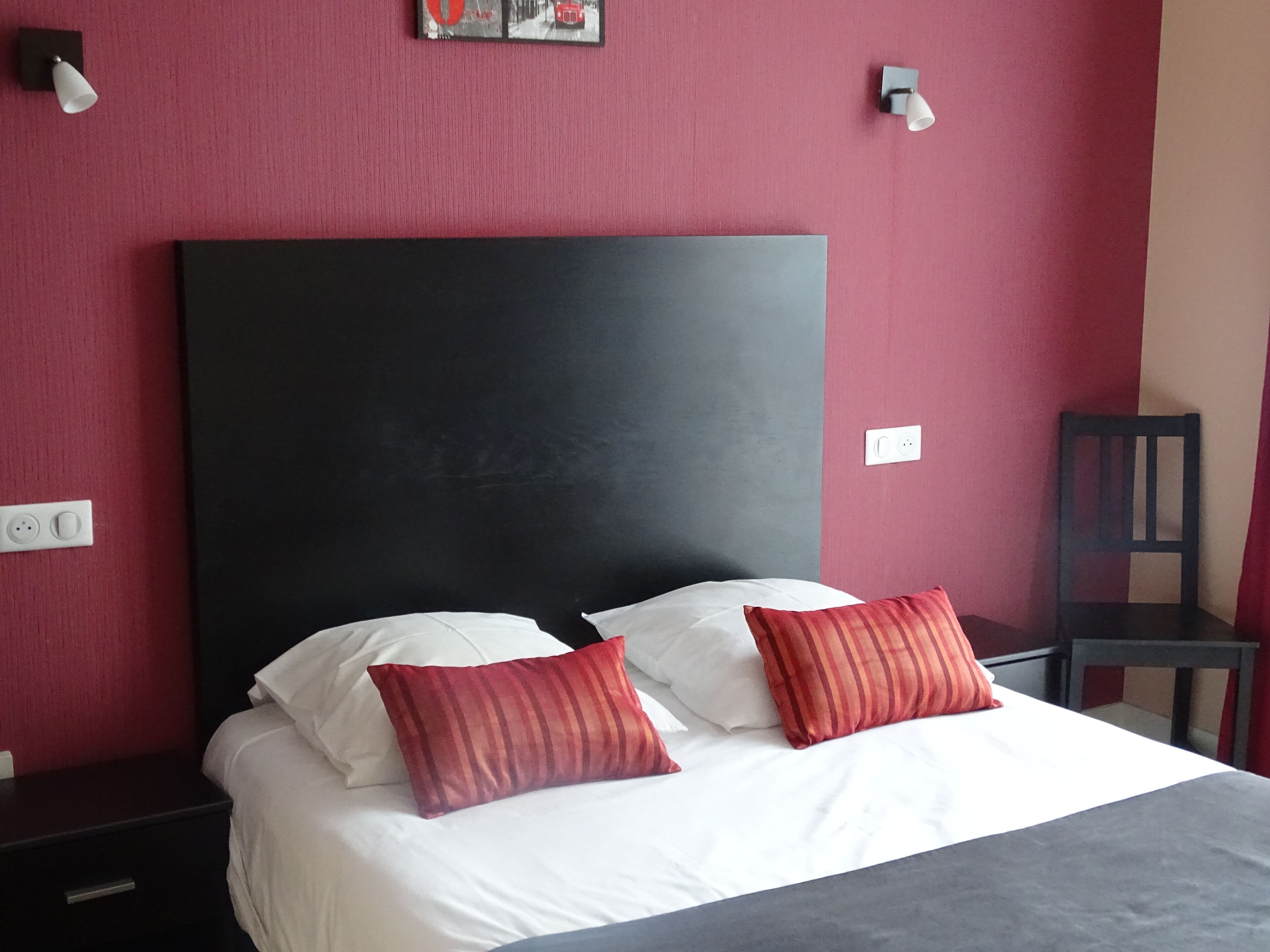 A hotel room with a large bed, two bedside tables, a nightstand, a chair, and a wall-mounted picture.