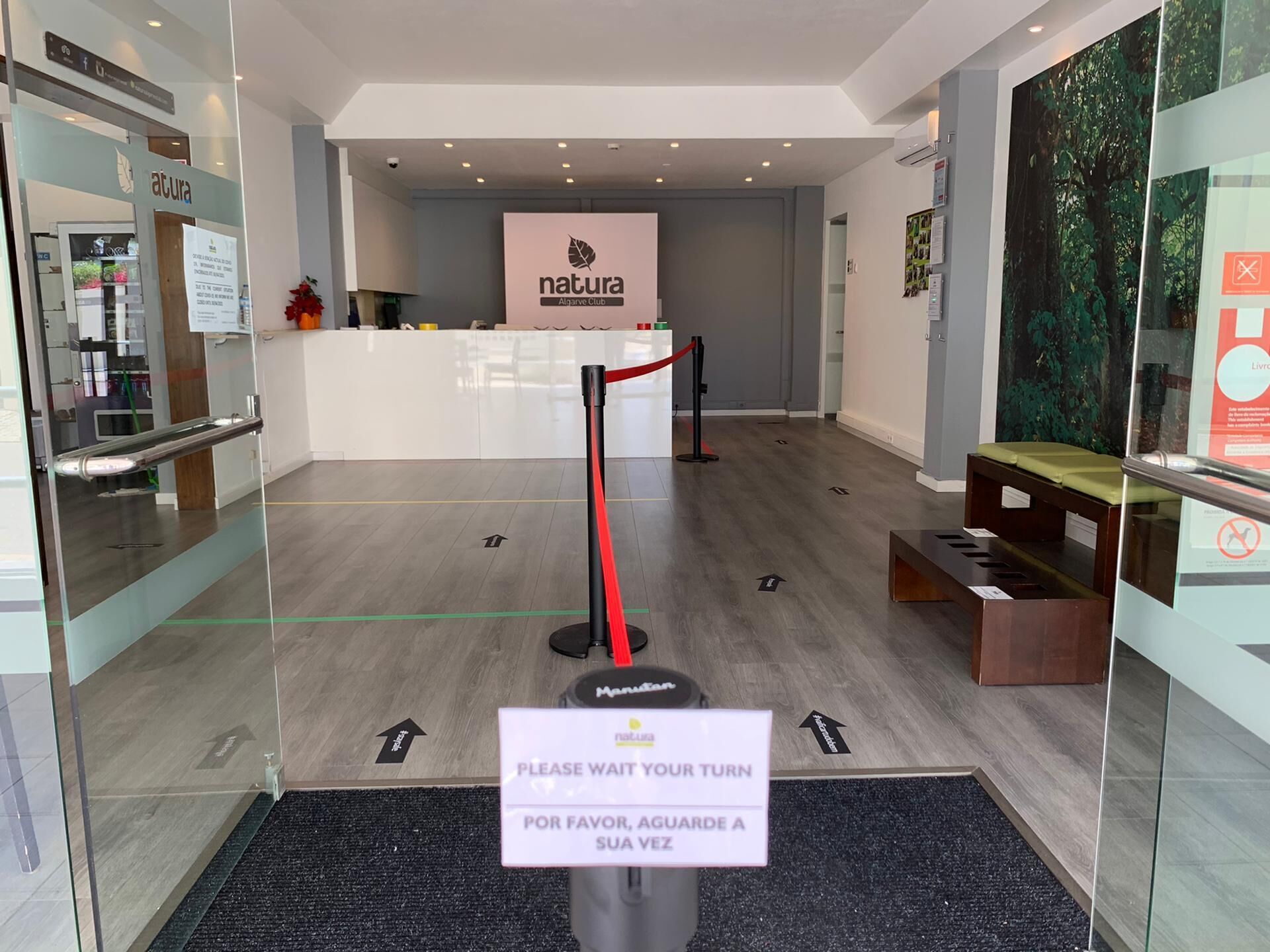 A reception area with a sign reading "Please wait your turn" and "Por favor, aguarde a su vez".