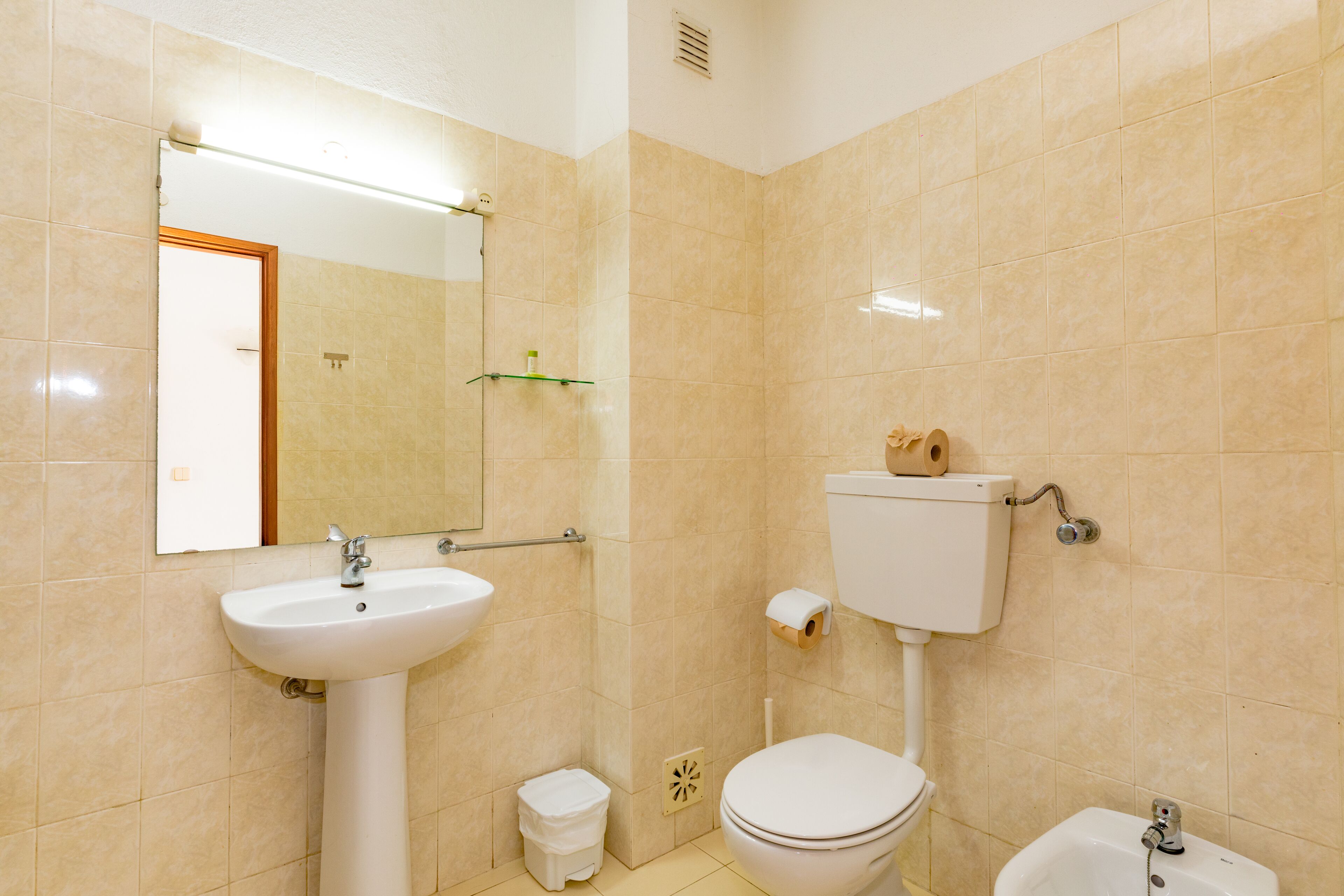 Un baño con baldosas color beige, un lavabo blanco, un inodoro y un bidé.