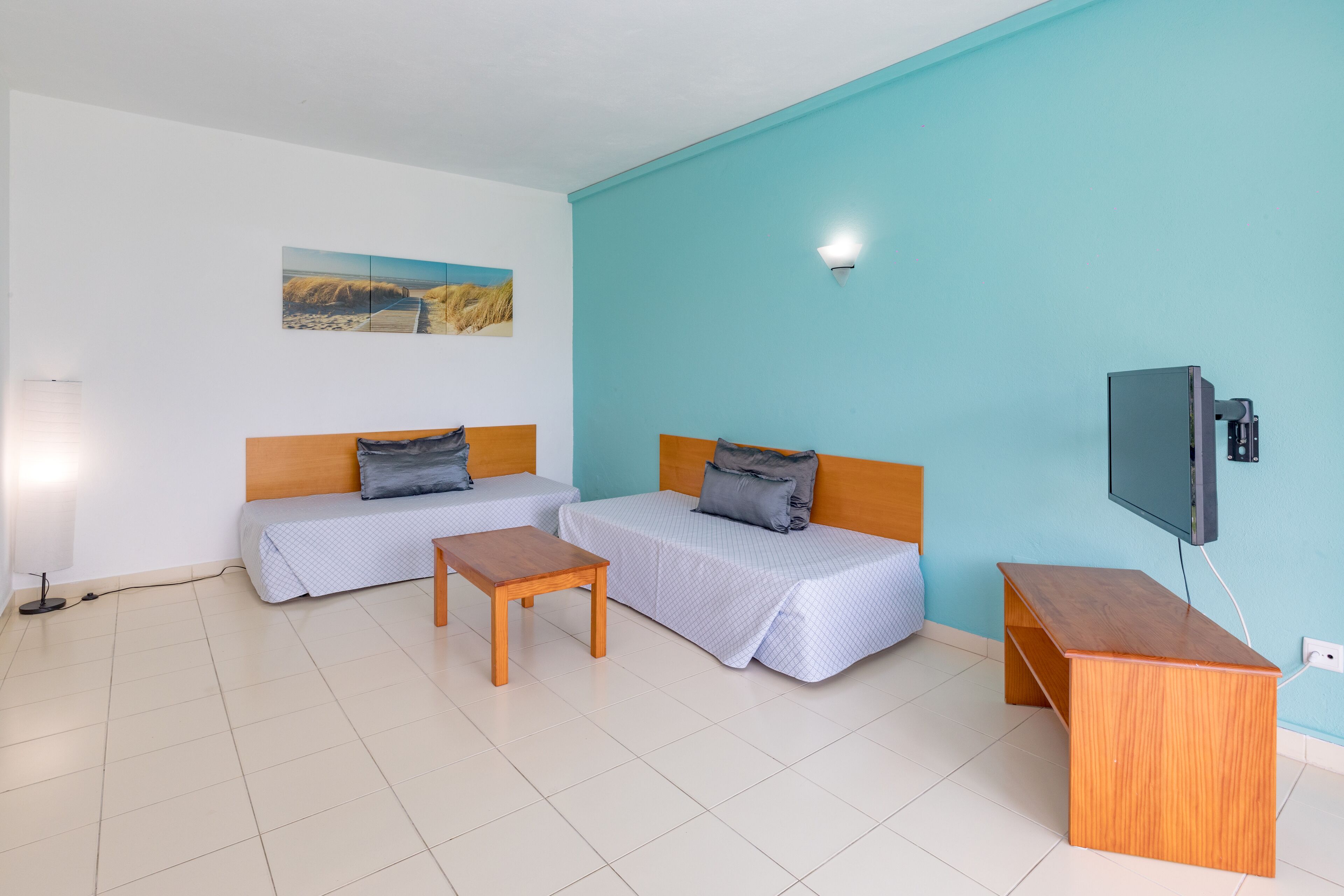 Ein Zimmer mit zwei Betten, einem Schreibtisch, einem Fernseher und einem Gemälde an der Wand.