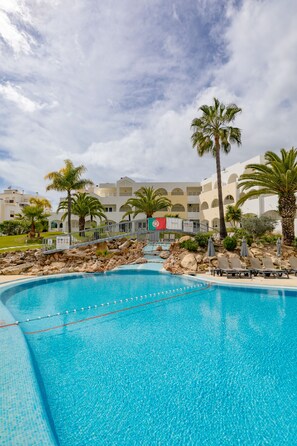 A swimming pool with clear blue water, surrounded by palm trees and a building with balconies in the background. - Natura Algarve Club (Albufeira)