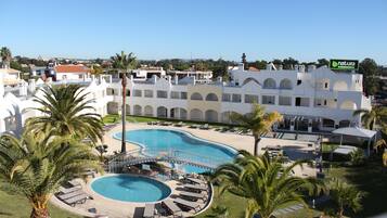 A resort with a large swimming pool, palm trees, and a view of the surrounding area.