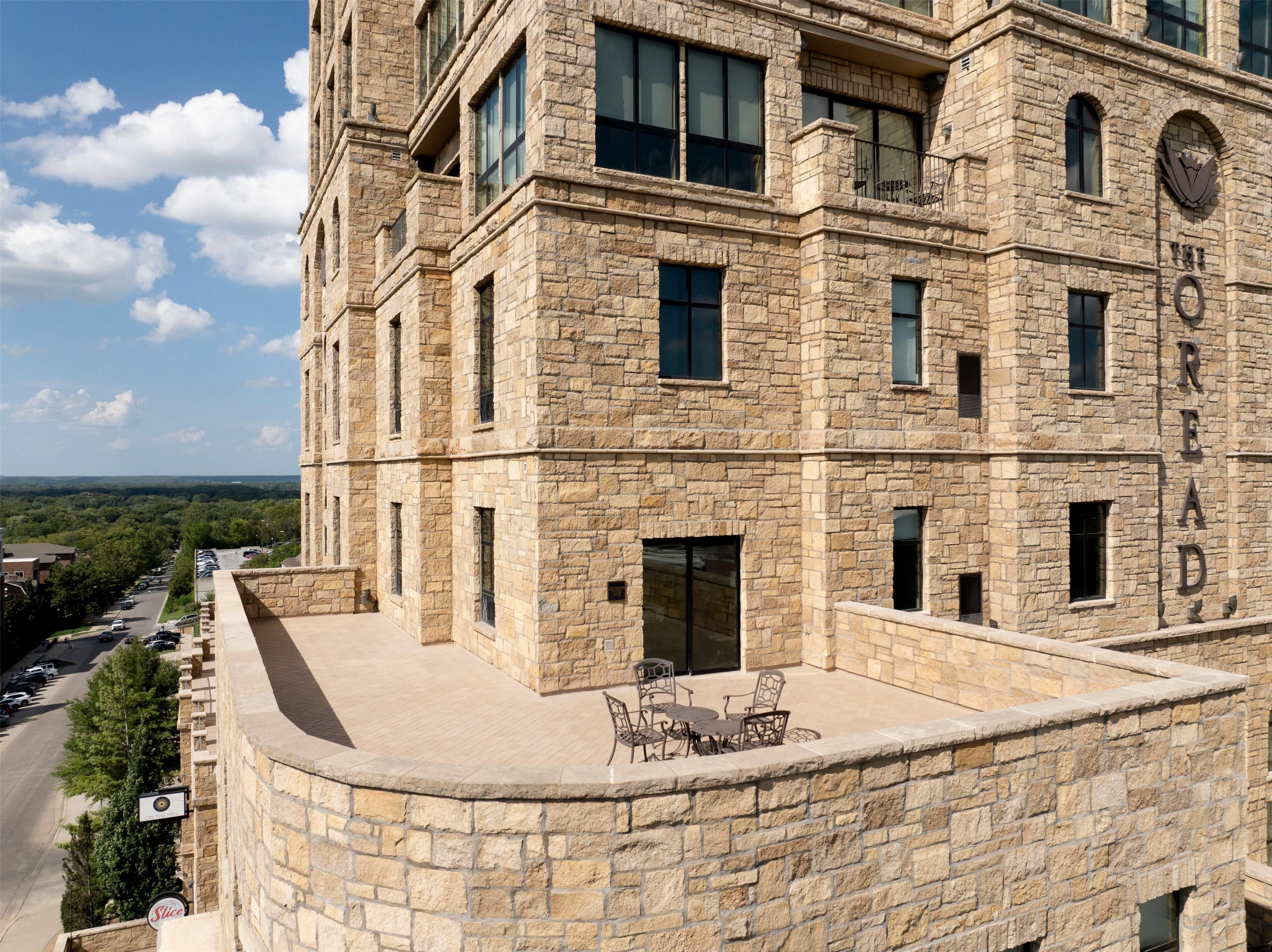 A stone building with a rooftop patio, multiple windows, and a view of the surrounding area.