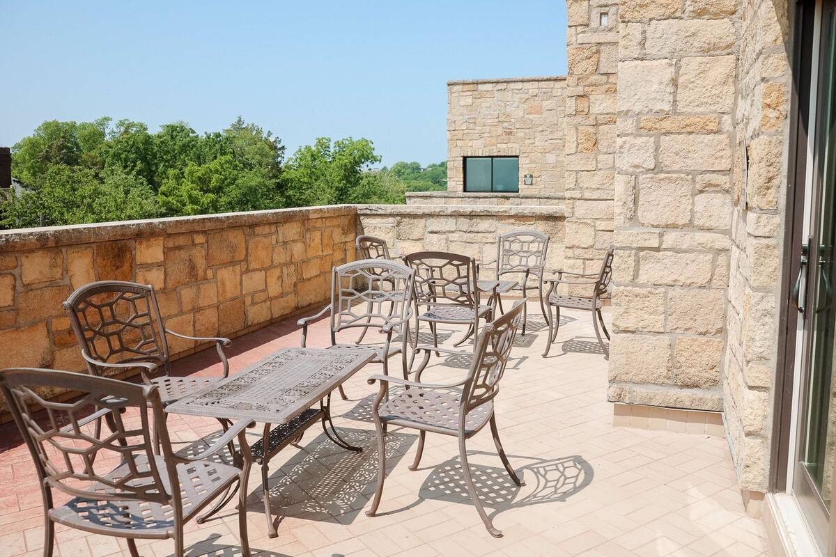 Terraza en la azotea con mobiliario exterior, pared de piedra y vista a zonas verdes.