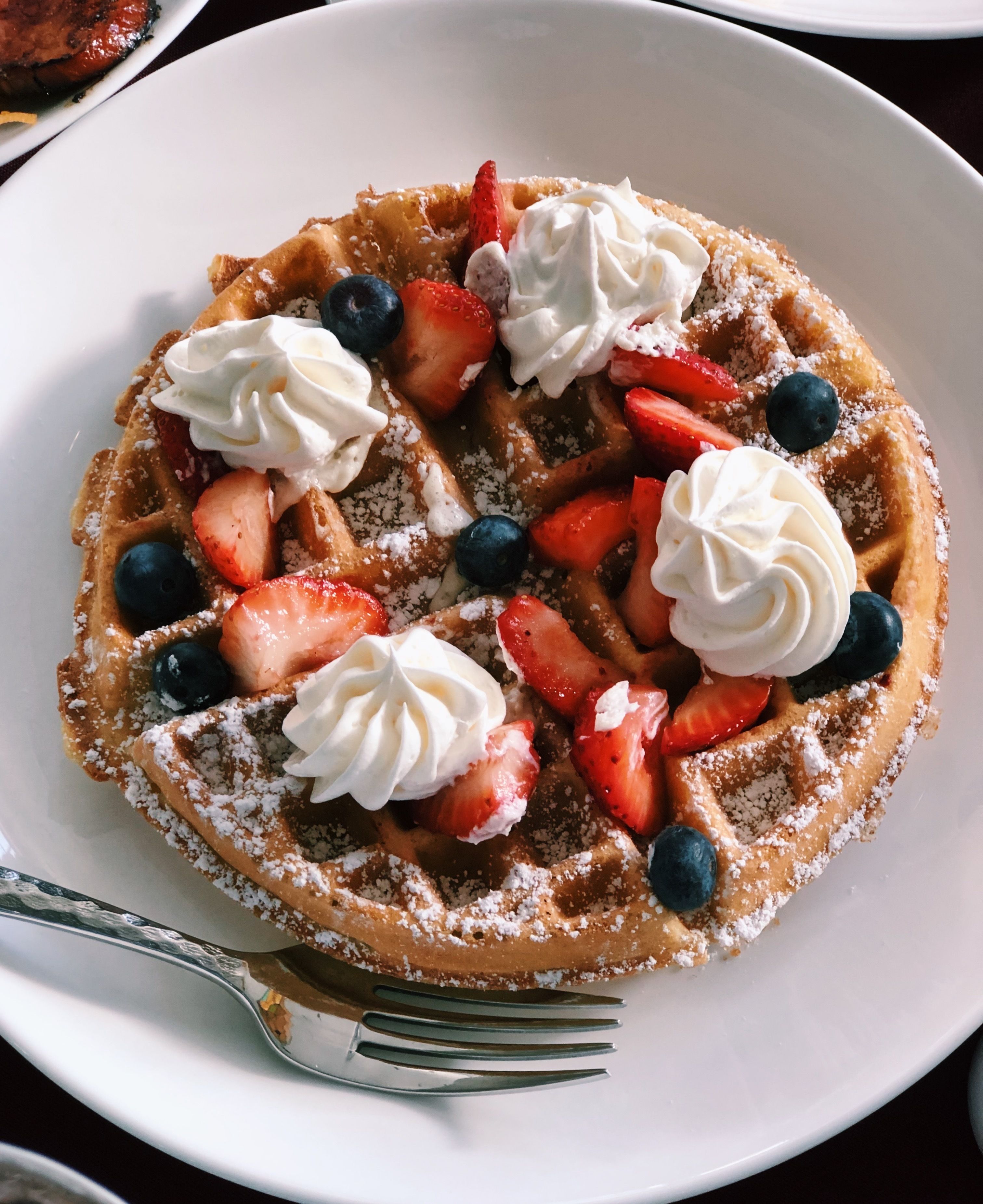 A plate of waffles topped with whipped cream, strawberries, and blueberries.