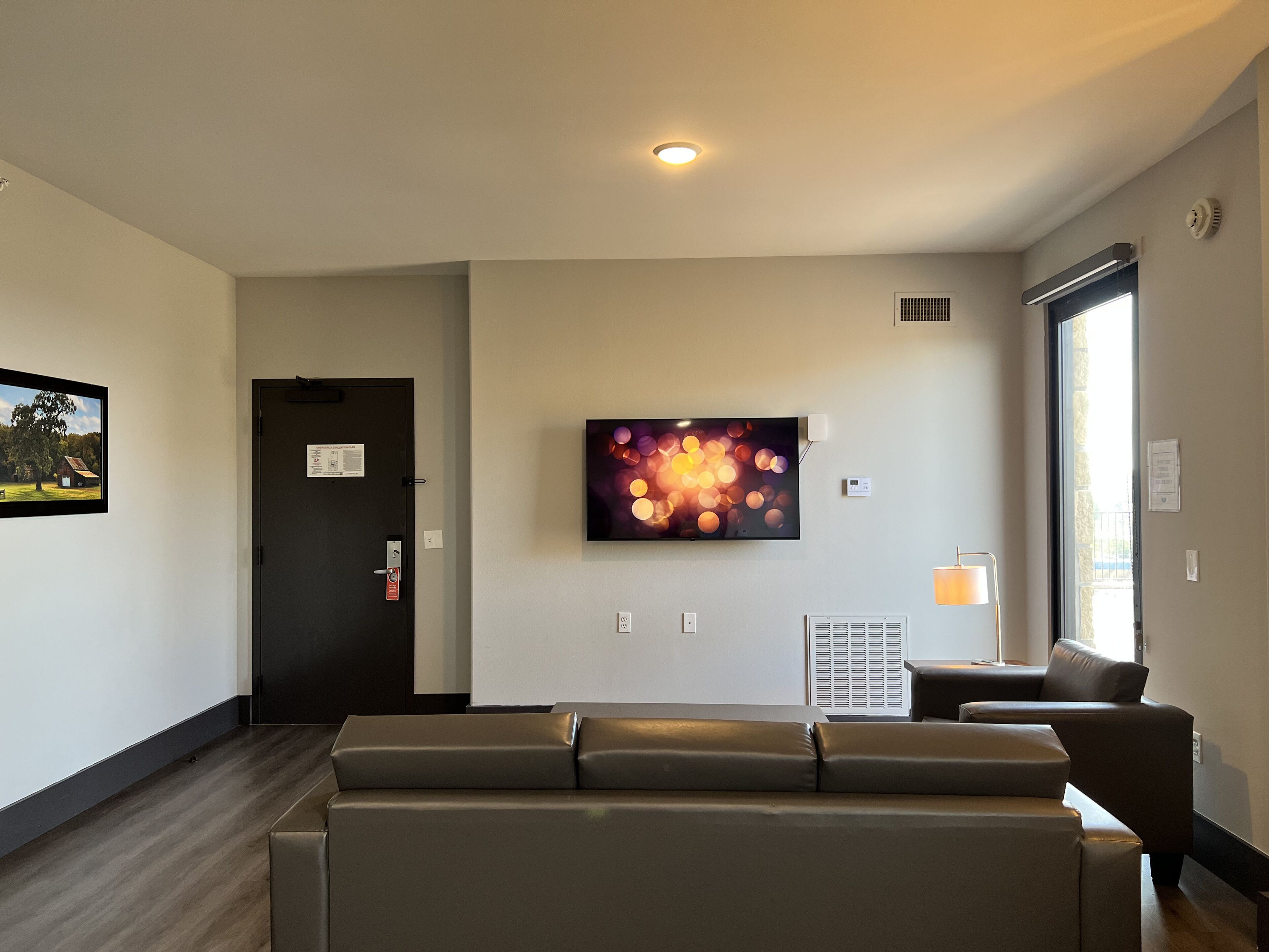 Um hall de hotel moderno com uma receção, uma grande TV de ecrã plano na parede, uma área de estar com um sofá e uma janela que proporciona luz natural.