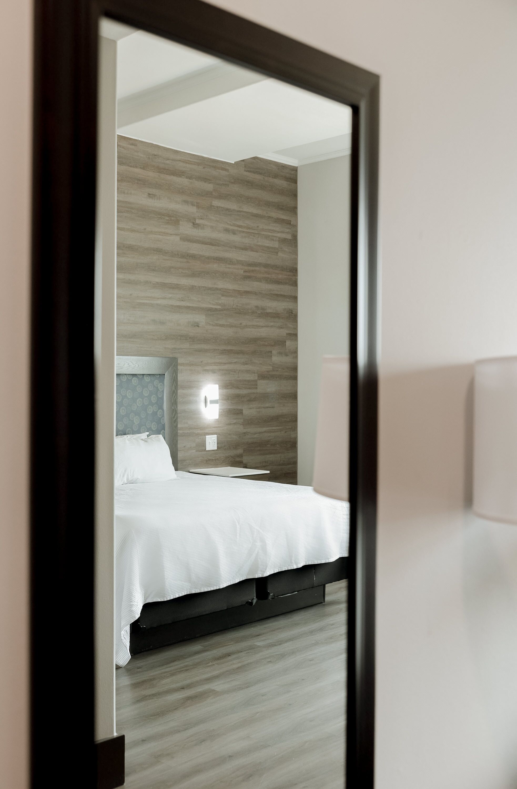 Una habitación de hotel moderna con un cabecero de madera, una cama con sábanas blancas y una mesita de noche.